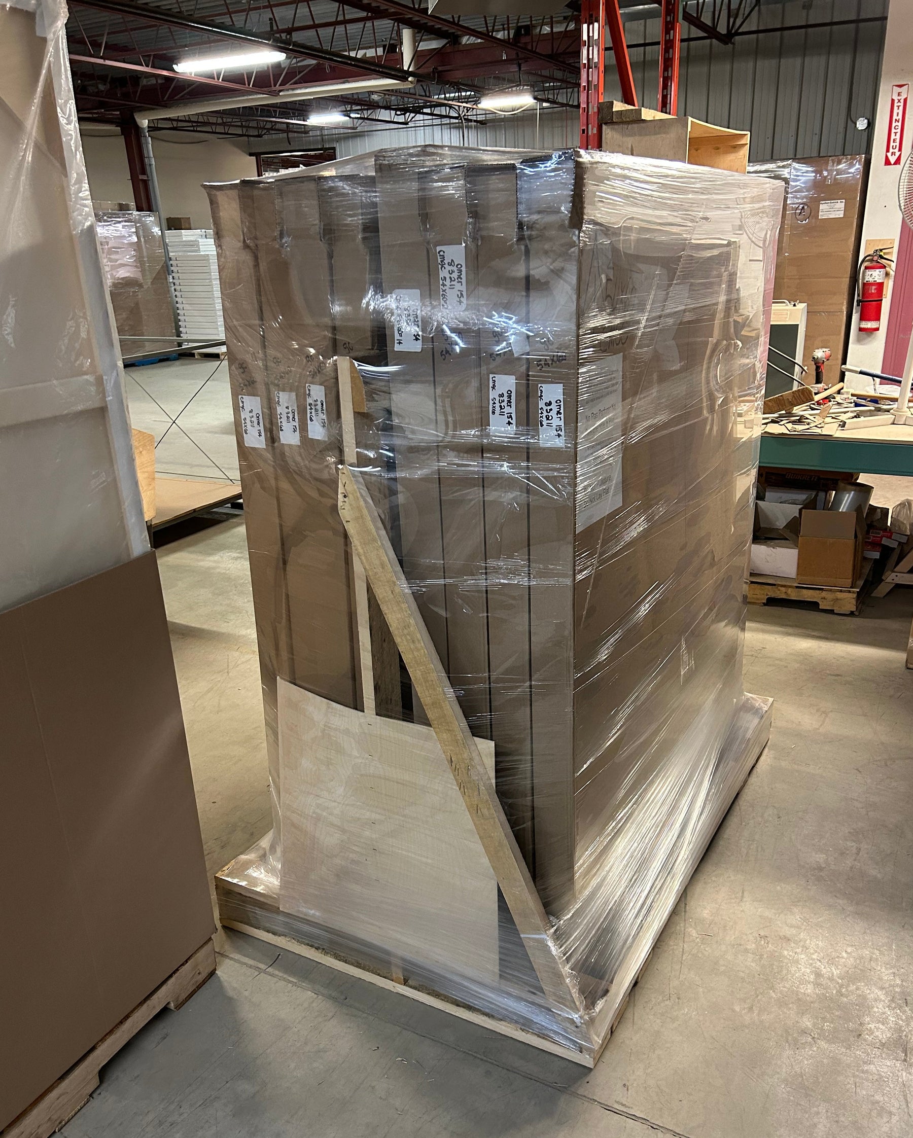 A large pallet stacked with tall brown cardboard boxes and wrapped in clear plastic, sitting on a concrete floor in the Apollon warehouse.