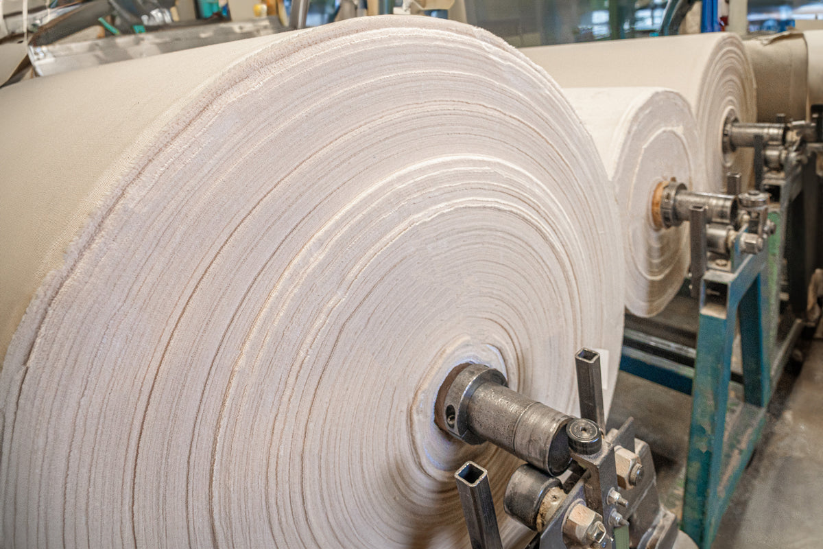 Grands rouleaux industriels de toile de coton, enroulés sur des broches métalliques en usine