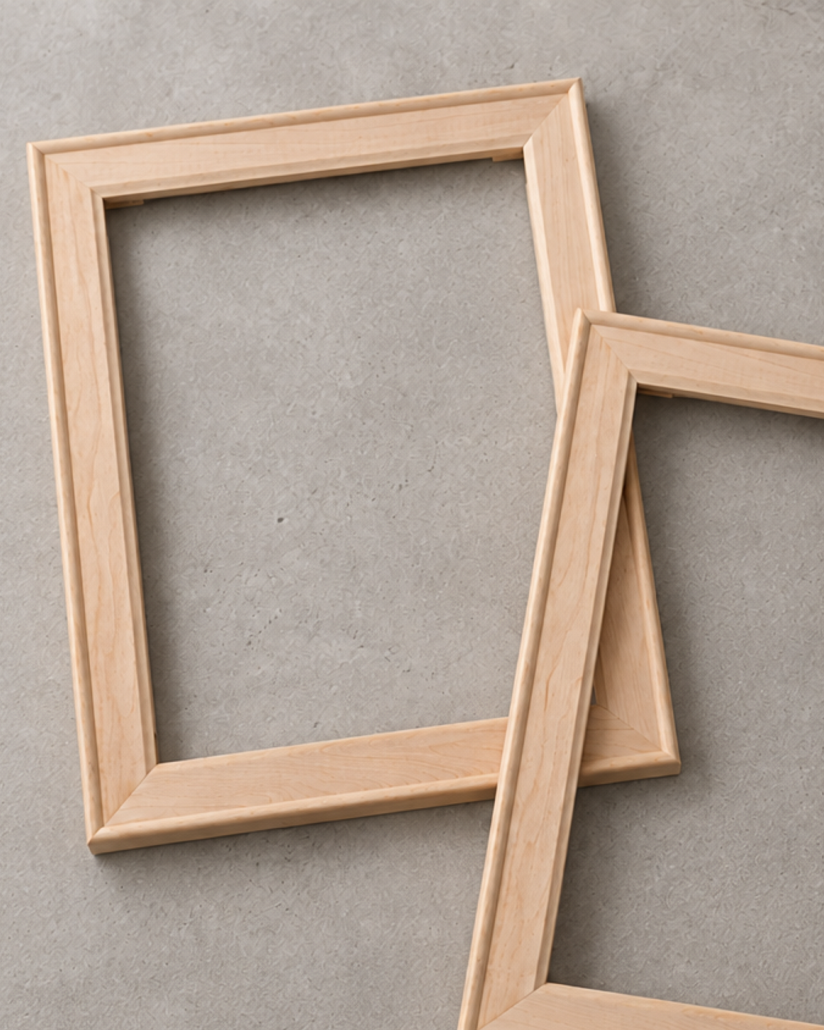 Unfinished wooden stretcher frames leaning against a neutral concrete background.